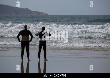 Due surfisti che indossano mute nere che si affacciano sul mare su Una spiaggia di Lanzada, o Grove Foto Stock