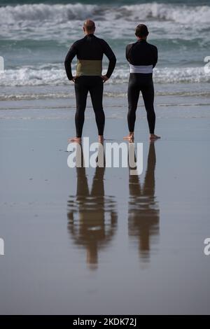 Due surfisti che indossano mute nere che si affacciano sul mare su Una spiaggia di Lanzada, o Grove Foto Stock