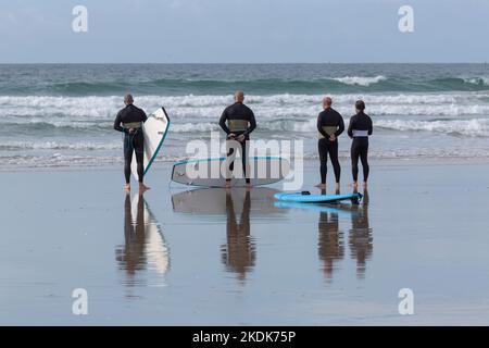 Un gruppo di surfisti con tavole da surf apprendista blu e mute nere su Una spiaggia di Lanzada, o Grove Foto Stock