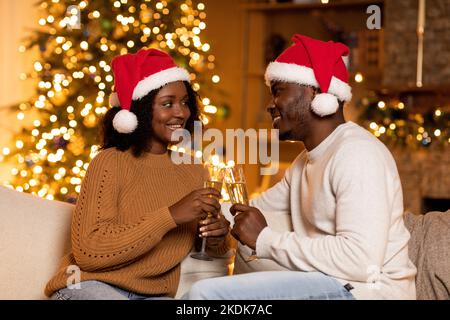 Una giovane coppia afro-americana sorridente a Babbo Natale, si acclama con un bicchiere di champagne Foto Stock