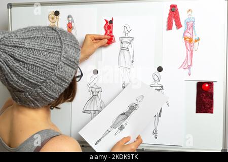 Il sarto disegna gli abiti. Il fashion designer sviluppa schizzi di abbigliamento femminile alla moda. Luogo di lavoro da marinaio. Foto Stock