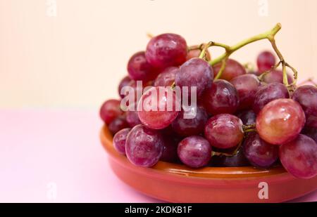 Immagine di un mazzo di uve viola in una pentola di argilla rotonda su sfondo neutro con spazio copia Foto Stock