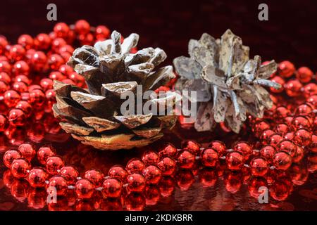 Decorazione natalizia con due coni di pino e una ghirlanda rossa su sfondo rosso brillante. Foto Stock