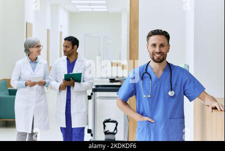 Operatore sanitario sorridente in uniforme blu con stetoscopio in piedi davanti al corridoio dell'ospedale. dipendenti medici Foto Stock