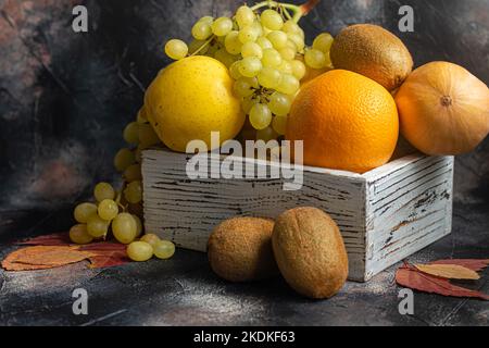 Mele gialle, kiwi con uva, arancio in una scatola di legno bianca. Autunno set di frutta. Copia spazio Foto Stock