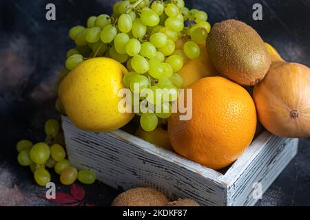 Mele gialle, kiwi con uva, arancio in una scatola di legno bianca. Autunno set di frutta. Copia spazio Foto Stock