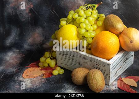 Mele gialle, kiwi con uva, arancio in una scatola di legno bianca. Autunno set di frutta. Copia spazio Foto Stock