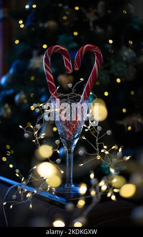 vetro vuoto di cristallo in cui si trovano i lollipop rossi a forma di cuore. ghirlande incandescenti e bokeh dall'albero festivo. atmosfera festosa del nuovo anno ho Foto Stock