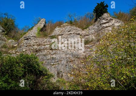 Alte scogliere calcaree, in parte arruffate, con ingressi nelle grotte e ingressi artificiali per le miniere di piombo, a Middleton Dale, Stoney Middleton, Peak District. Foto Stock