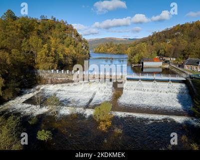 Ripresa aerea della diga sul lago Katrine con diverse chiuse aperte e acqua che scende lungo la scala dei pesci in una bella giornata autunnale. Foto Stock