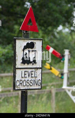 Vintage, Old Level Crossing Sign con un'immagine di un treno a vapore e un triangolo di avvertimento di fronte A Una serie di segnali, Inghilterra, Regno Unito Foto Stock