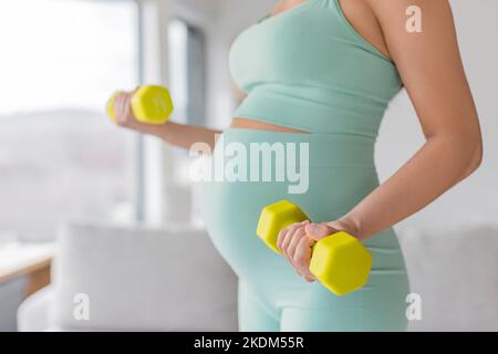 Donna incinta formazione prenatale a casa facendo esercizio di fitness forza con pesi manubri. Corpo braccio di allenamento ricci closeup di pancia e. Foto Stock