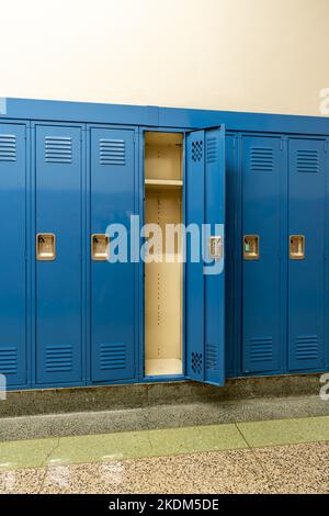 Singolo armadietto in metallo blu vuoto aperto lungo un corridoio non descritto in una tipica scuola superiore americana. Nessuna informazione identificabile inclusa nella sala. Foto Stock