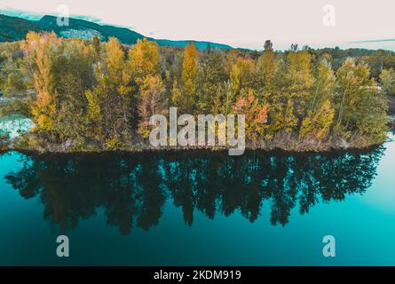 Il riflesso degli alberi in autunno sulla superficie dell'acqua, colorate foglie giallo-arancio. La foresta che riflette nella superficie di acqua. Lago blu-turchese Foto Stock