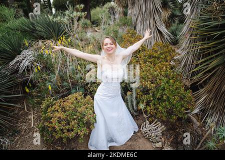 Sposa fare Airplane ali con le braccia in un giardino di Cactus Foto Stock