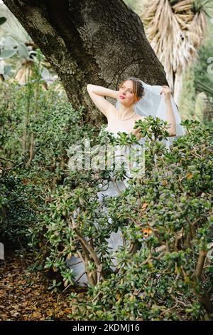 Sposa che si appoggia contro l'albero di quercia in un giardino di Cactus Foto Stock