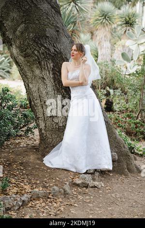 Sposa che si appoggia contro l'albero di quercia in un giardino di Cactus Foto Stock