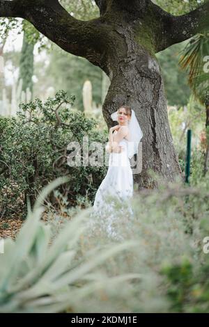 Sposa che si appoggia contro l'albero di quercia in un giardino di Cactus Foto Stock