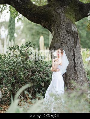 Sposa che si appoggia contro l'albero di quercia in un giardino di Cactus Foto Stock