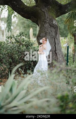 Sposa che si appoggia contro l'albero di quercia in un giardino di Cactus Foto Stock