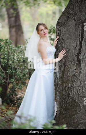 Sposa che si appoggia contro l'albero di quercia in un giardino di Cactus Foto Stock