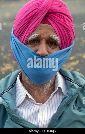 Ritratto posto di un uomo Sikh più anziano in un turbante rosa e maschera parziale. Sulla 74th Street a Jackson Heights, Queens, New York City. Foto Stock