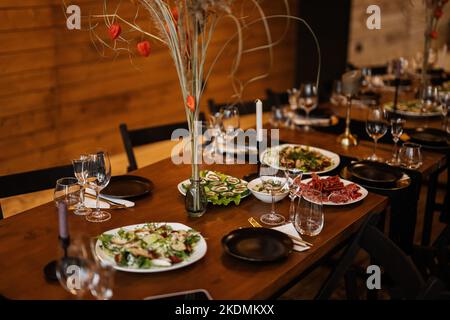 Grande, lungo, decorato, tavolo e sedie in legno, coperto di piatti, fiori, candele. Foto Stock