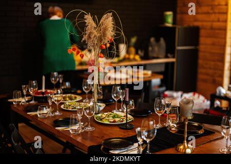 Grande, lungo, decorato, tavolo e sedie in legno, coperto di piatti, fiori, candele. Foto Stock