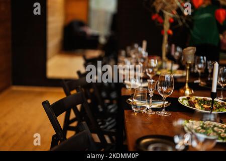 Grande, lungo, decorato, tavolo e sedie in legno, coperto di piatti, fiori, candele. Foto Stock