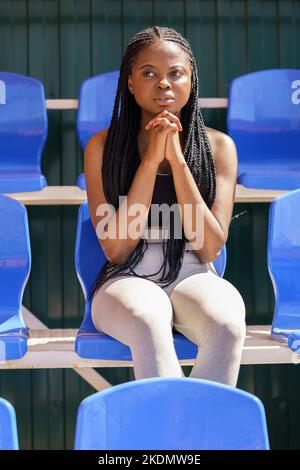 Giovane ragazza afro-americana prega si siede su stand di strada stadio e guarda in lontananza Foto Stock