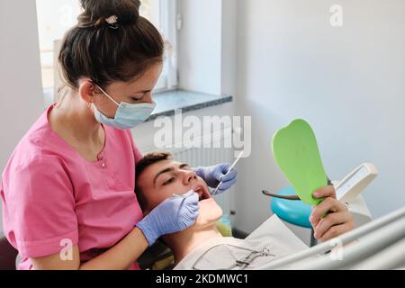 Il dentista esamina la condizione dei denti con l'aiuto dello specchio dentale nei pazienti. Il concetto di igiene orale professionale. Foto Stock