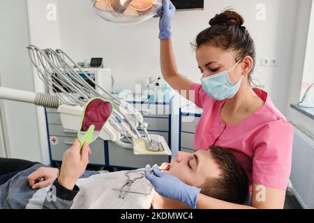 Il dentista esamina la condizione dei denti con l'aiuto dello specchio dentale nei pazienti. Il concetto di igiene orale professionale. Foto Stock