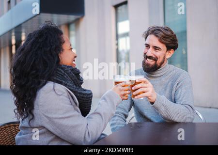 Una giovane coppia multietnica brinda e beve birra in un bar della città, godendosi il suo tempo libero. Concetto di stile di vita. Foto Stock