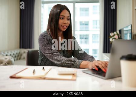Ritratto di una donna d'affari positiva che lavora su un computer portatile alla sua scrivania a casa Foto Stock