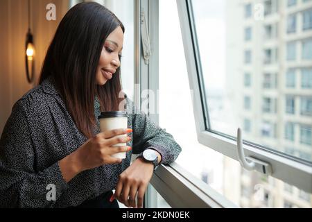 Elegante donna d'affari sorridente godendo di vista dal suo appartamento in grattacielo Foto Stock