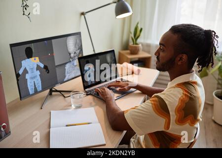 Vista laterale dell'uomo nero creativo che costruisce modelli 3D digitali sul luogo di lavoro dell'ufficio domestico Foto Stock
