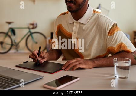 Primo piano dell'uomo nero creativo che utilizza la tavoletta grafica sul posto di lavoro per il design digitale o l'editing di foto, spazio di copia Foto Stock