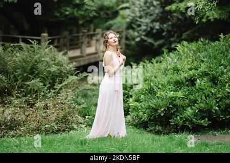 Donna che indossa un abito rosa che legge un libro in un giardino idilliaco Foto Stock