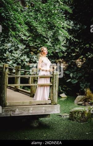 Donna che indossa un abito rosa che legge un libro in un giardino idilliaco Foto Stock