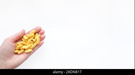 Struttura in primo piano di compresse multivitaminiche gialle in mano femminile su sfondo bianco. Concetto di stile di vita sano Foto Stock