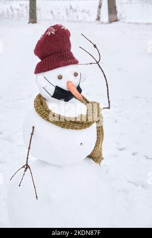 Un pupazzo di neve perplesso in un cappello e sciarpa a maglia con una maschera protettiva indossata in modo errato. Foto Stock