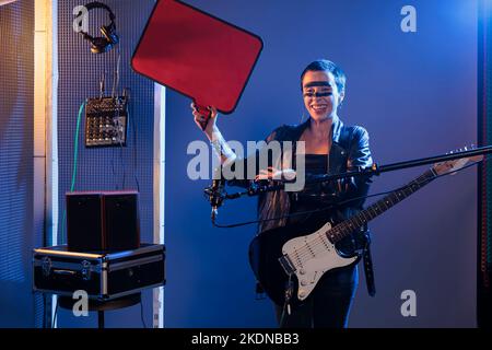 Ragazza felice del bilanciere che tiene la bolla di discorso del cartone e la chitarra per fare pubblicità al messaggio del testo sul bordo isolato del cartone del mockup. Mostrare il cartellone vuoto prima di perfezionare la musica heavy metal. Foto Stock
