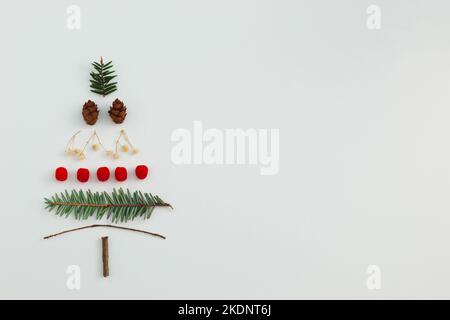 Albero di Natale fatto con abete sempreverde, coni di pino, bacche rosse e rami su sfondo bianco. Composizione minima di appartamento di vacanza. Inverno creativ Foto Stock