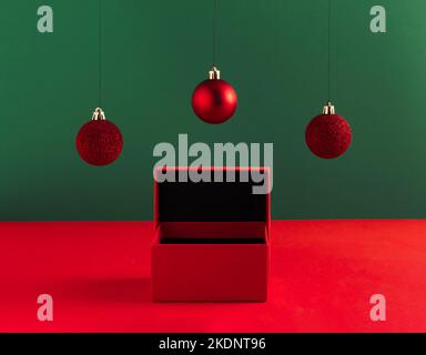 Concetto creativo di Natale fatto di scatola regalo e baubles rosso su sfondo verde audace. Concetto minimo di annuncio di Capodanno. Mostra mock up per i professionisti Foto Stock