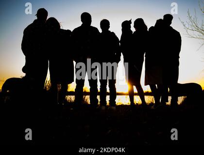 Silhouette di un gruppo di persone che guardano il tramonto di fronte ad un lago. Foto Stock