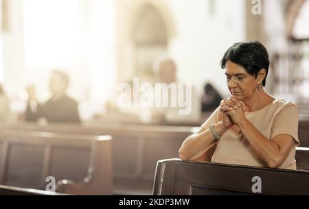 Donna anziana che prega in chiesa, adorare e fidarsi di Dio, la preghiera o il rispetto spirituale. La donna cristiana lode nel tempio santo della religione, della fede e. Foto Stock