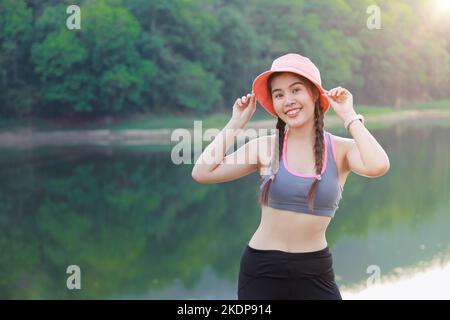 sport sana donna asiatica in piedi all'aperto sorriso felice carino con sfondo foresta lago Foto Stock
