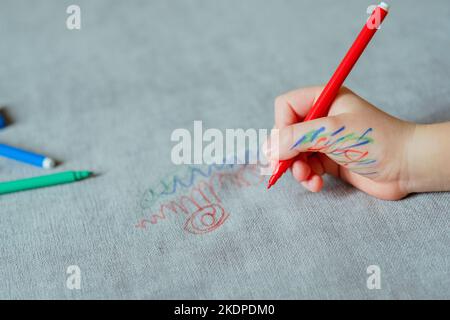 Un bambino si è macchiato di mano d'inchiostro, disegnando con un contrassegno rosso sul rivestimento del lettino. Tessuto per mobili. Concetto di pulizia Foto Stock