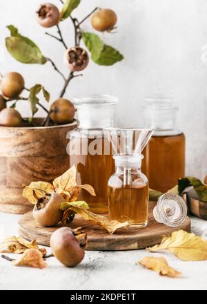 Sciroppo di nespola fatto in casa o succo in tre bicchieri da farmacia con frutta fresca matura su tagliere di legno. Concetto di medicina alternativa. Foto Stock