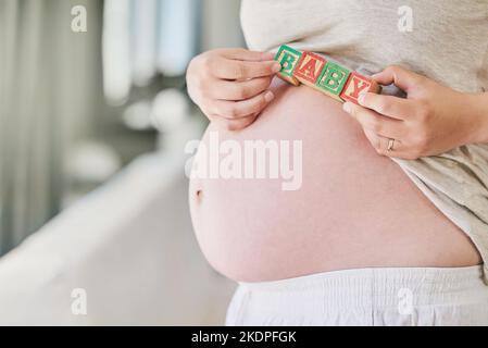 Theres un bambino sul senso. Una donna che tiene i blocchi di costruzione contro il suo ventre incinta. Foto Stock